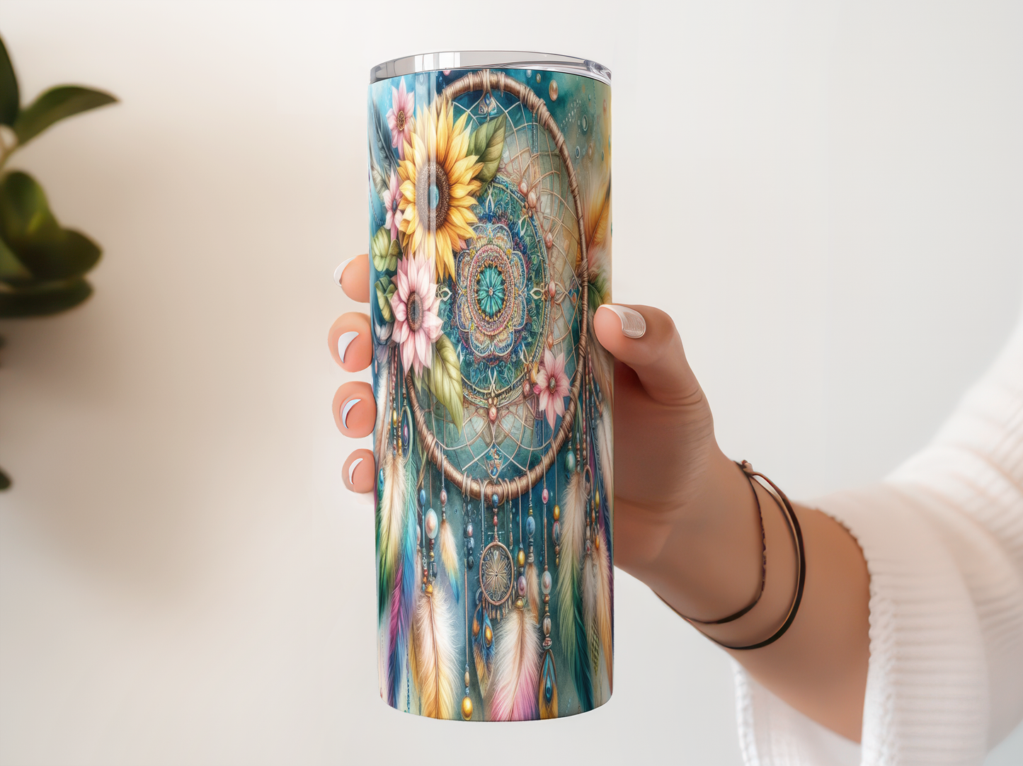A person's hand holding a colorful, patterned tumbler or cup with a dreamcatcher design.