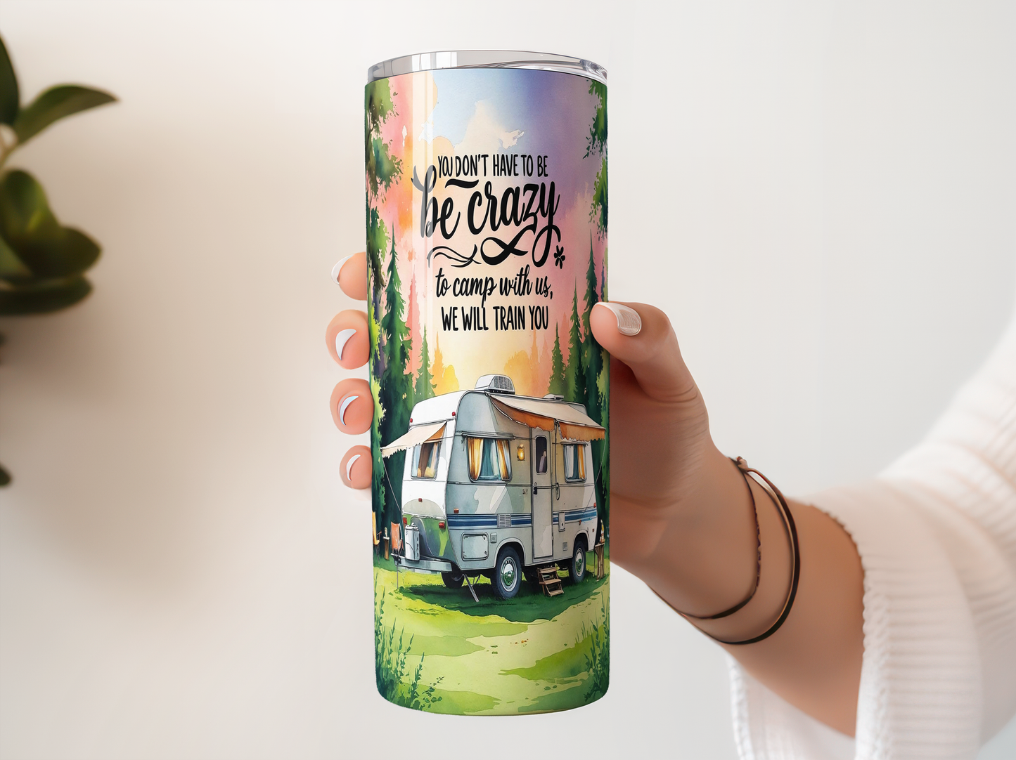 A person's hand holding a tall, cylindrical container with a colorful design featuring a camper van and a forest scene.