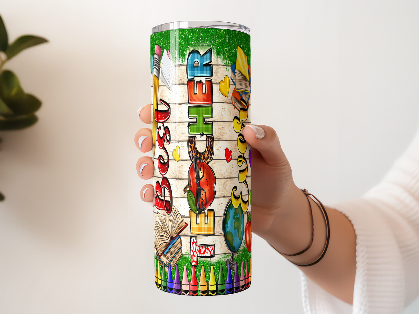 A person's hand holding a colorful, patterned tumbler or cup with various school-related and educational-themed designs on it.