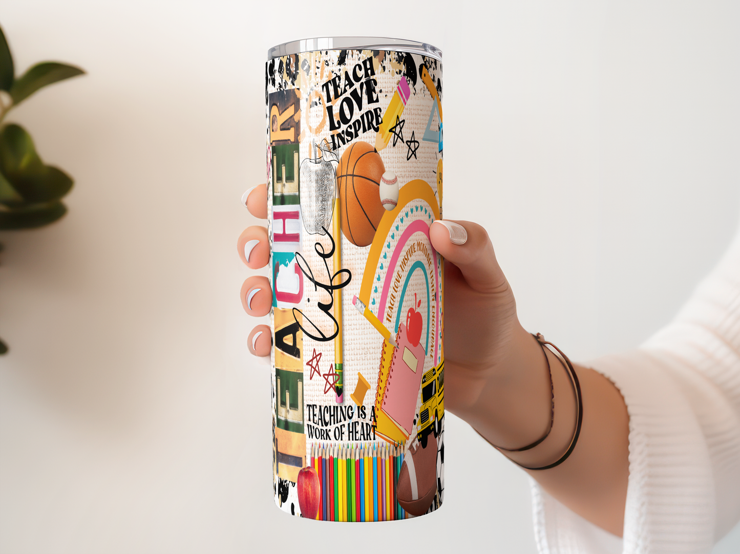 A person's hand holding a colorful, decorated tumbler or cup with various school-related and teacher-related designs and text.