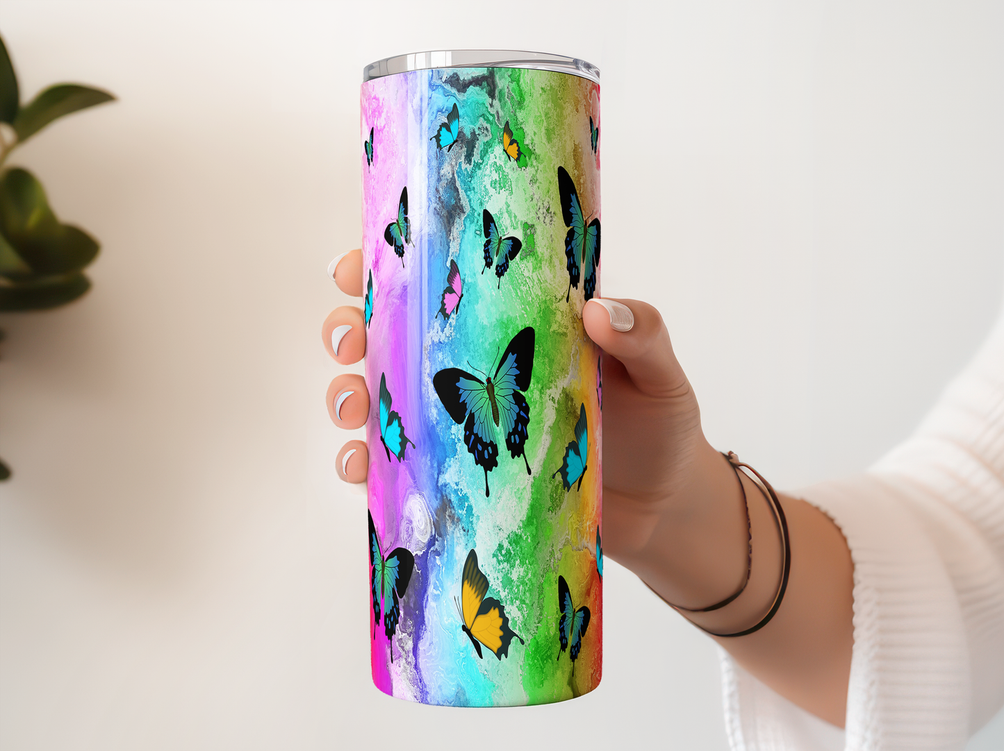 A person's hand holding a colorful, multicolored tumbler or cup with a butterfly design.