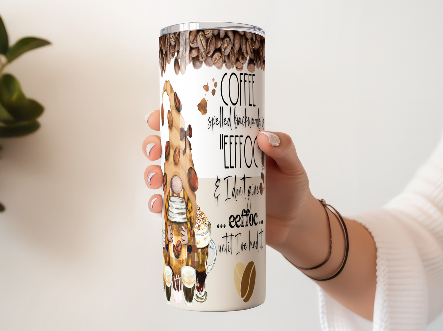 A person's hand holding a tall, cylindrical coffee cup with a design featuring coffee beans, a slice of pizza, and a person enjoying a beverage.