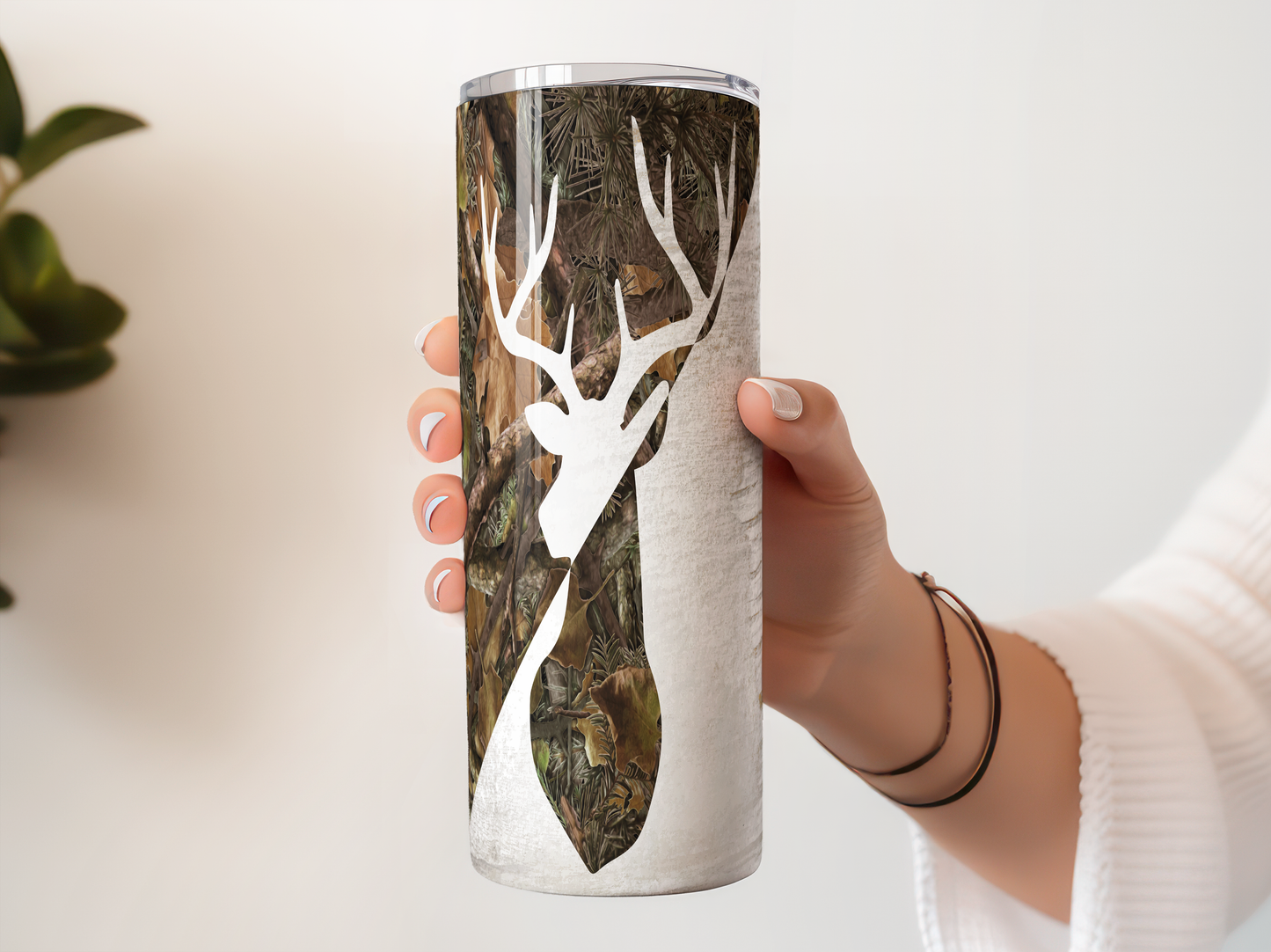 A person's hand holding a tall, cylindrical container with a camouflage pattern featuring a deer head silhouette.