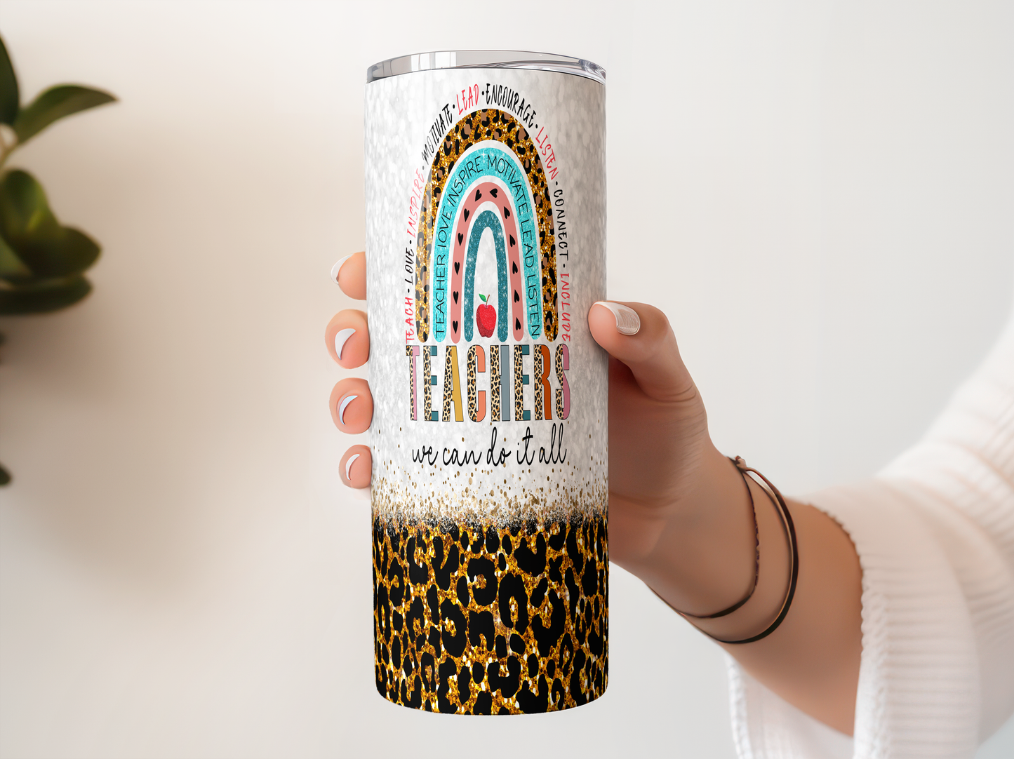 A person's hand holding a colorful tumbler with a leopard print pattern and a rainbow design.