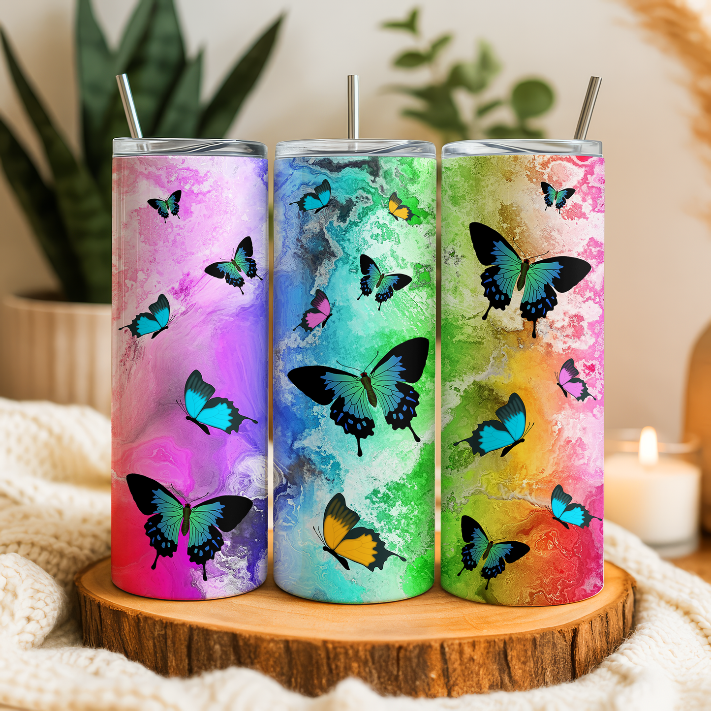 Three colorful tumblers with butterfly designs, placed on a wooden surface.